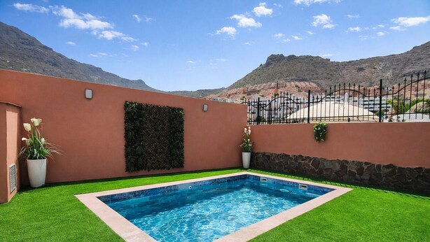 Una piscina rectangular rodeada de césped artificial, una pared de piedra y vistas a un paisaje montañoso.