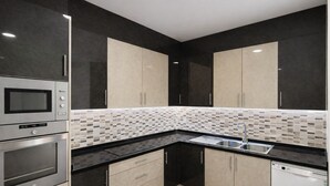 Una cocina moderna con armarios oscuros, salpicadero de azulejos y electrodomésticos de acero inoxidable.