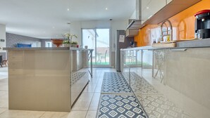 A modern kitchen with a central island, a dining area with a table and chairs, and a view through a glass door to the outside. - Spacious House with Garden & Terrace – Perfect for Families & Friends (Champcevinel)