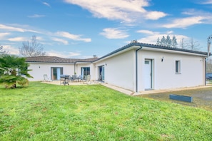 Une maison de plain-pied avec un patio, une petite pelouse et un ciel dégagé.