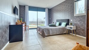 A modern bedroom with a bed, a desk, a TV, and a view of the outdoors. - Spacious House with Garden & Terrace – Perfect for Families & Friends (Champcevinel)