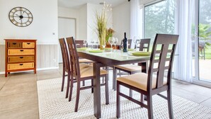 A dining area with a glass table, wooden chairs, a clock, and a view through large windows. - Spacious House with Garden & Terrace – Perfect for Families & Friends (Champcevinel)