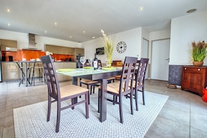 Un coin repas moderne avec une table dressée pour quatre personnes, entourée de chaises, dans une cuisine spacieuse dotée de placards et d’une horloge au mur.