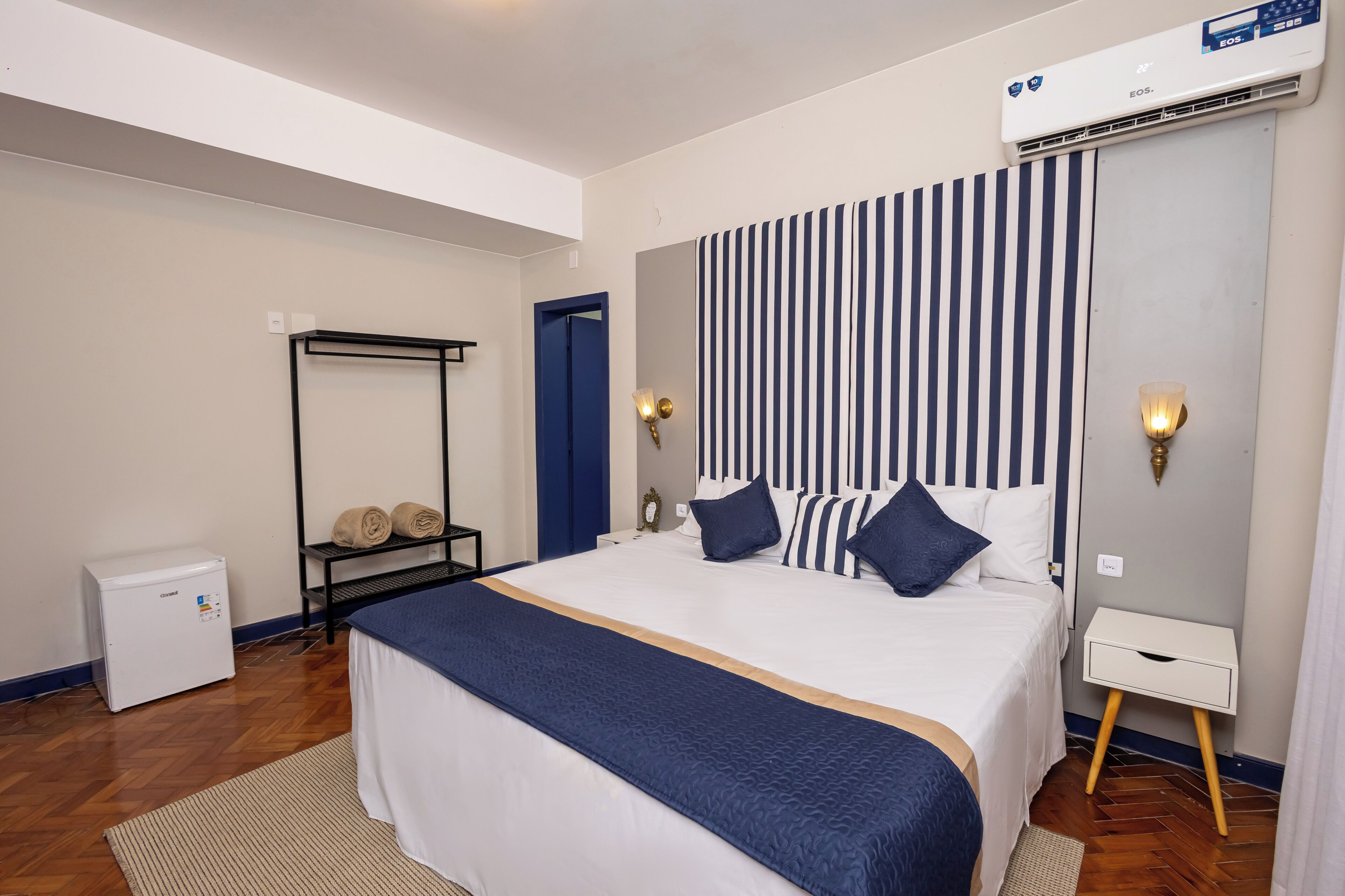 A hotel room with a large bed, a wardrobe, a small heater, and a wall-mounted air conditioner.