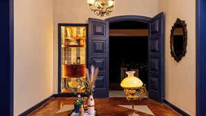 A hallway with a wooden floor, a chandelier, a lamp, and a mirror on the wall.
