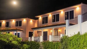 A two-story building with a balcony, illuminated windows, and a moon in the sky.