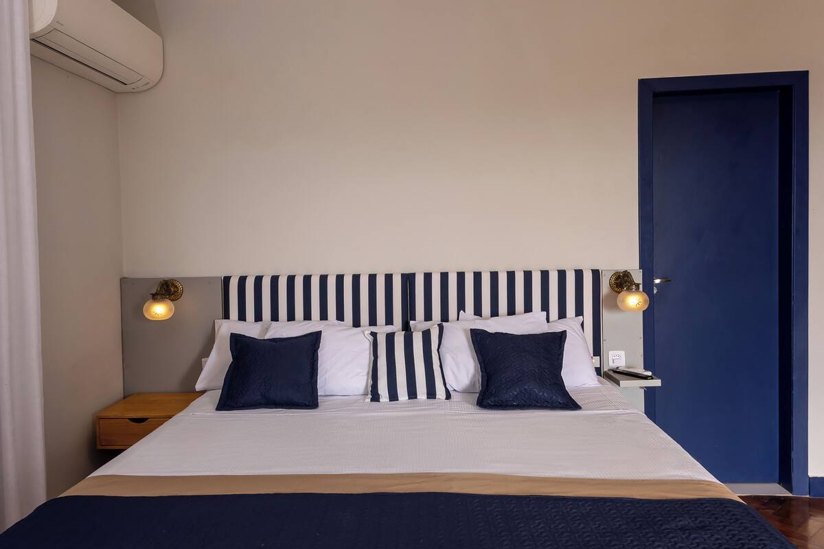 A neatly made bed with striped headboard and pillows, a bedside table with a lamp, and a blue door.