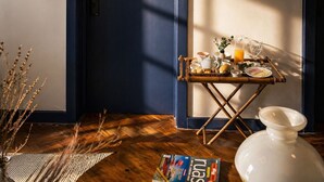 A room with a dark blue door, a bamboo table with breakfast items, a white vase, and a magazine on the floor.