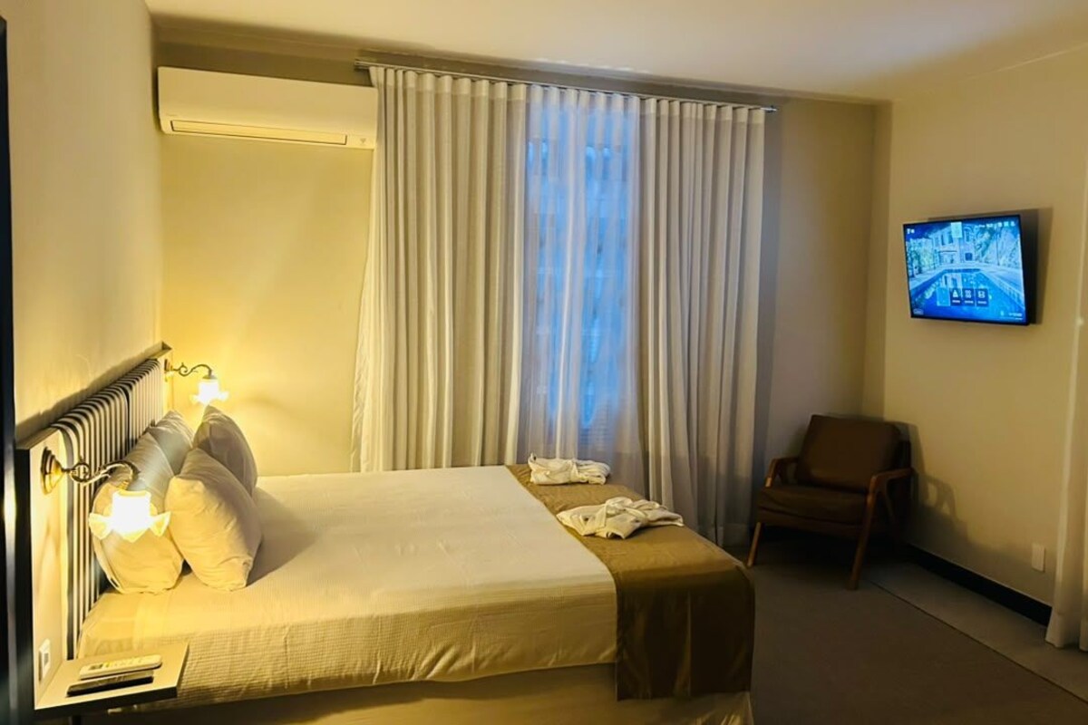 A hotel room with a bed, a chair, a television, and curtains.