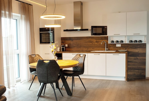 A modern kitchen with a dining area, featuring a wooden table, black chairs, a built-in oven, and a microwave. - Apartment-Fürstenau (Fürstenau)