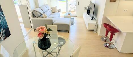 Una sala de estar moderna con una mesa de comedor de vidrio, sofás blancos y un taburete rojo.