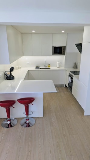 Une cuisine moderne avec des meubles blancs, un îlot central, des tabourets de bar rouges, un four à micro-ondes et une cuisinière.
