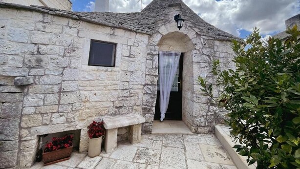 Un bâtiment en pierre avec une petite entrée, un banc et un pot de fleurs.