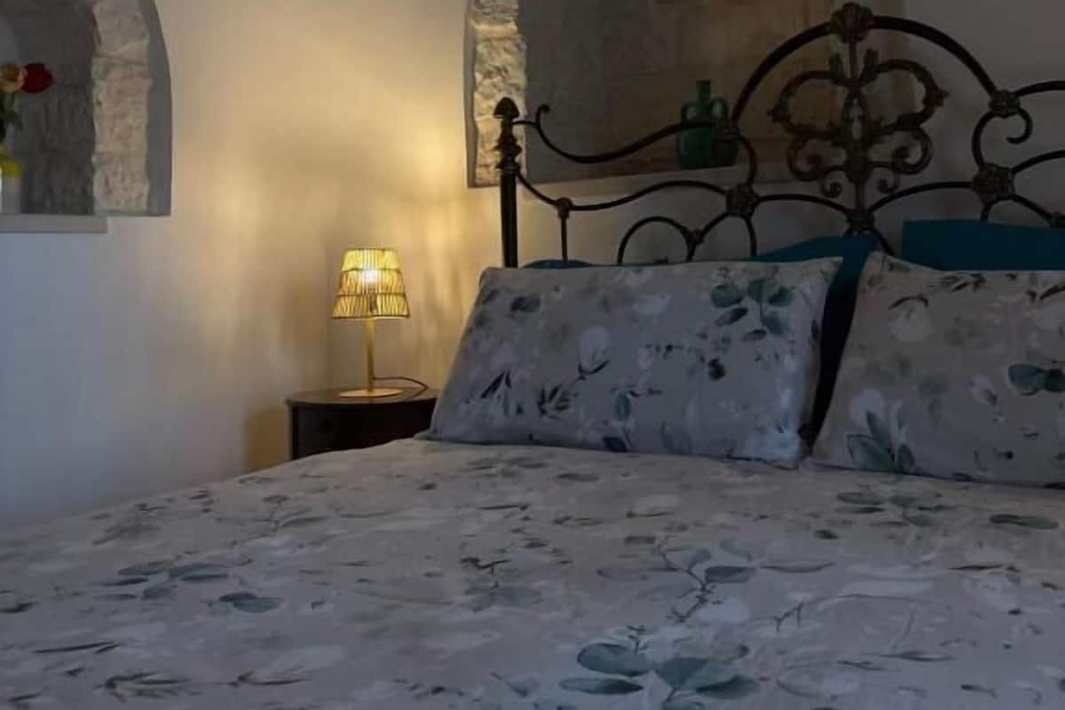 Ein Schlafzimmer mit einem Bett, einem Nachttisch, einer Lampe und Steinbögen an den Wänden.