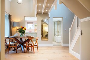 A dining area with a wooden table and chairs, a vase of flowers, and a mirror on the wall. - The Haybarn Banham Cottages (Bourton-on-the-Water)