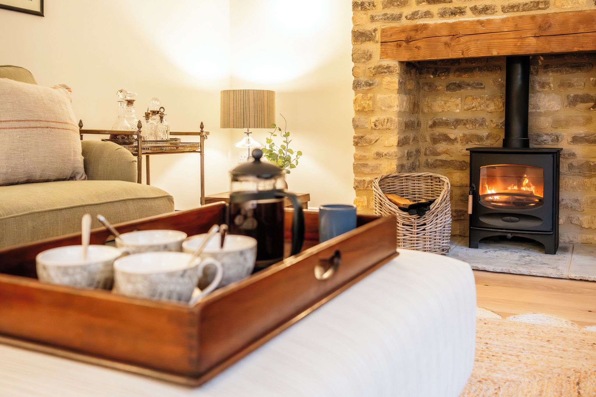 A cozy room with a stone fireplace, a bed, a wooden side table with a lamp, and a tray with cups and a kettle.