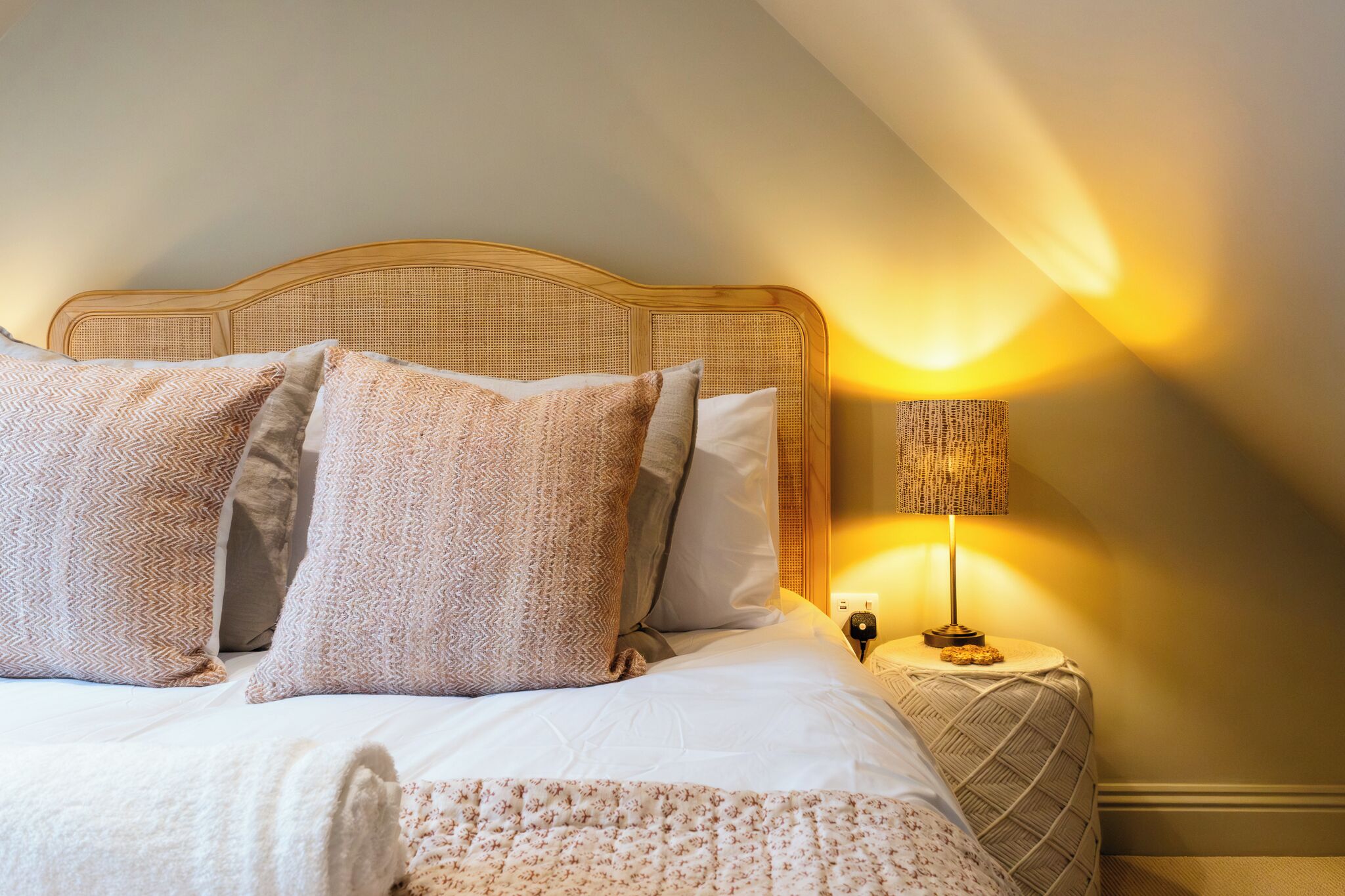 A neatly made bed with a headboard, pillows, and a bedside lamp.