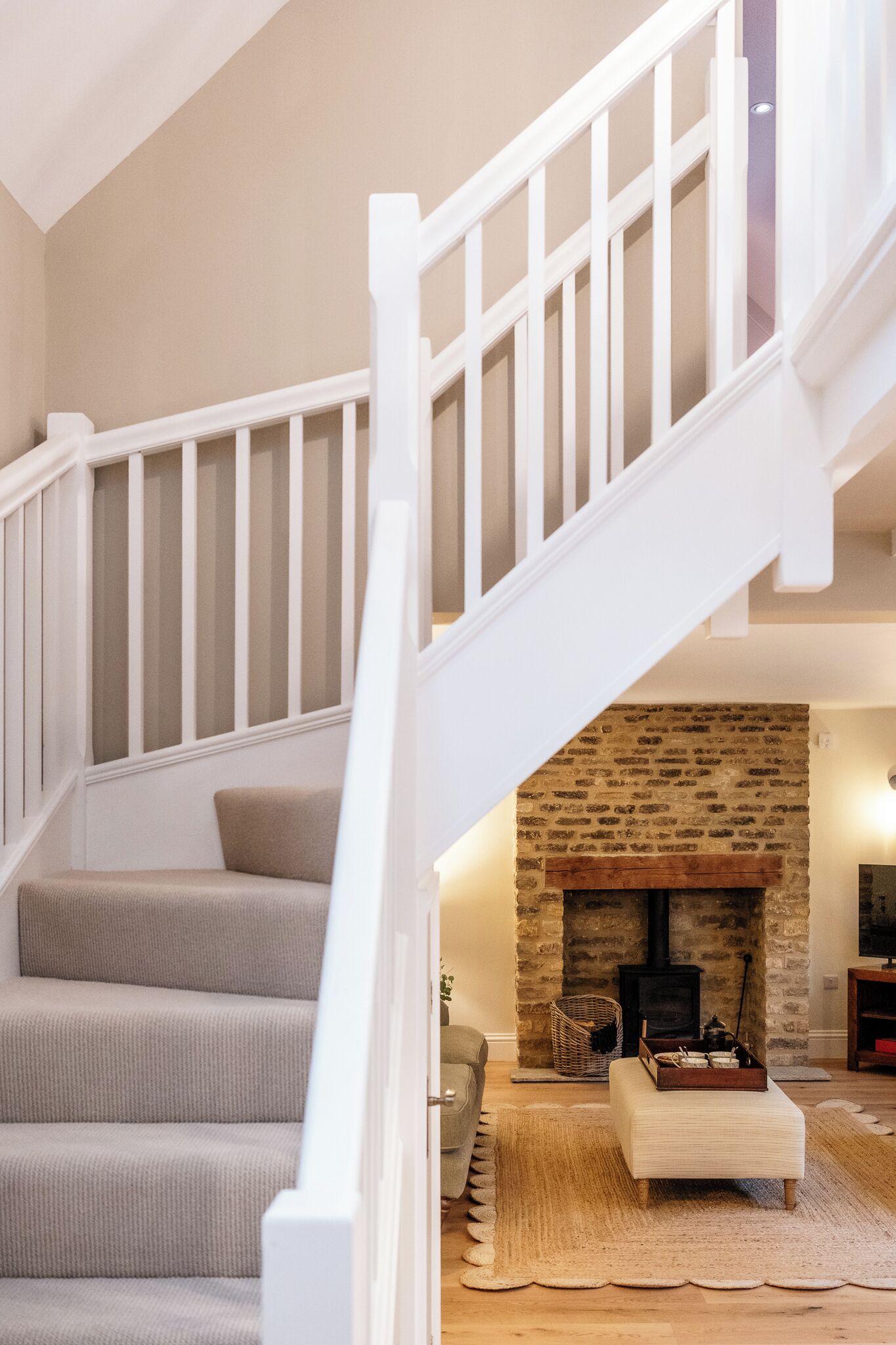 A staircase with white railings leading to a living area with a stone fireplace and a sofa.