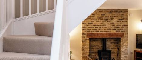 A staircase with white railings leading to a living area with a stone fireplace and a sofa.