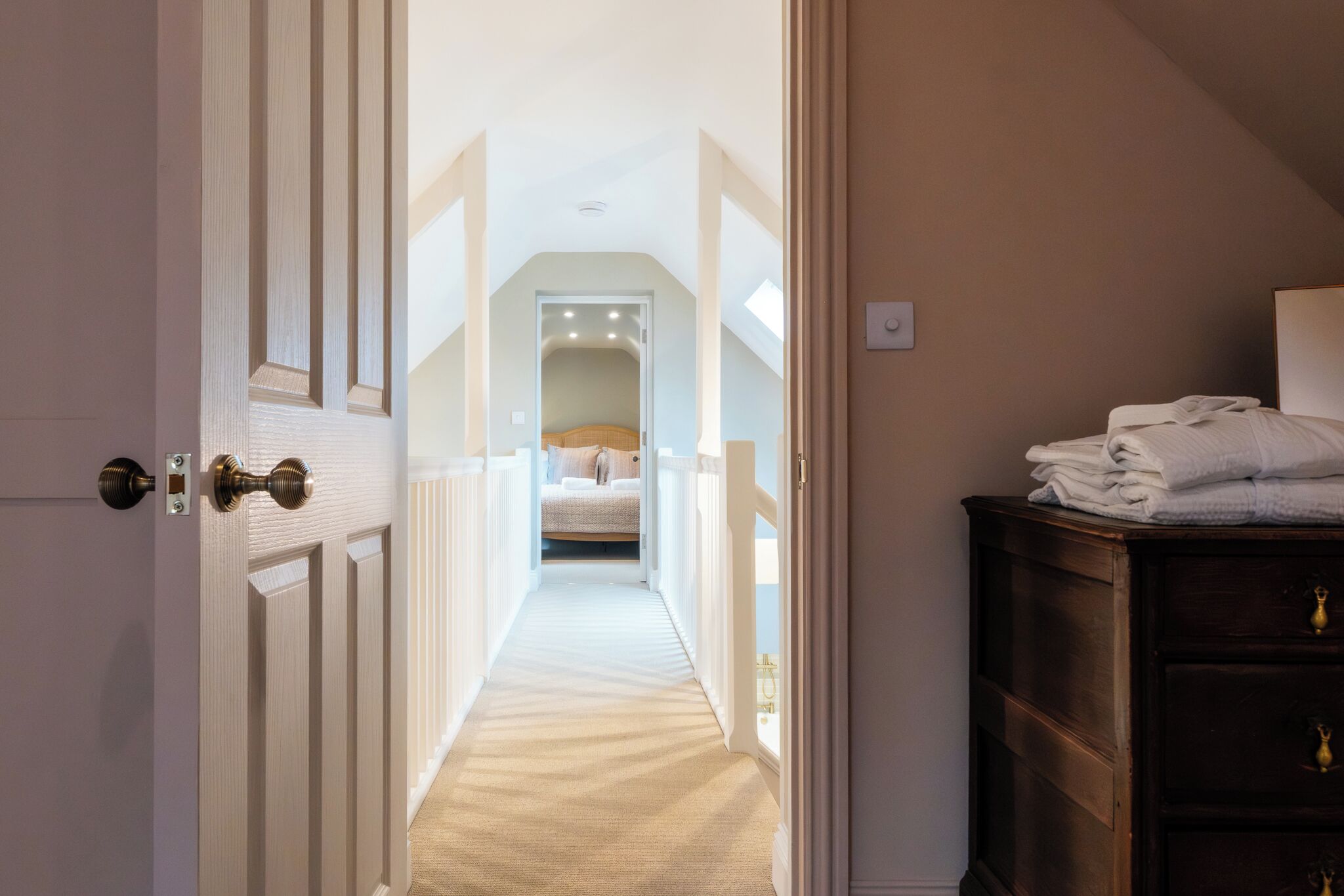 A hotel hallway leading to a bedroom with a bed, a dresser, and a door with a handle.