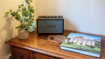 Un escritorio de madera con un altavoz Marshall, una planta en maceta y un libro titulado 'At Home in the Cotswolds'.