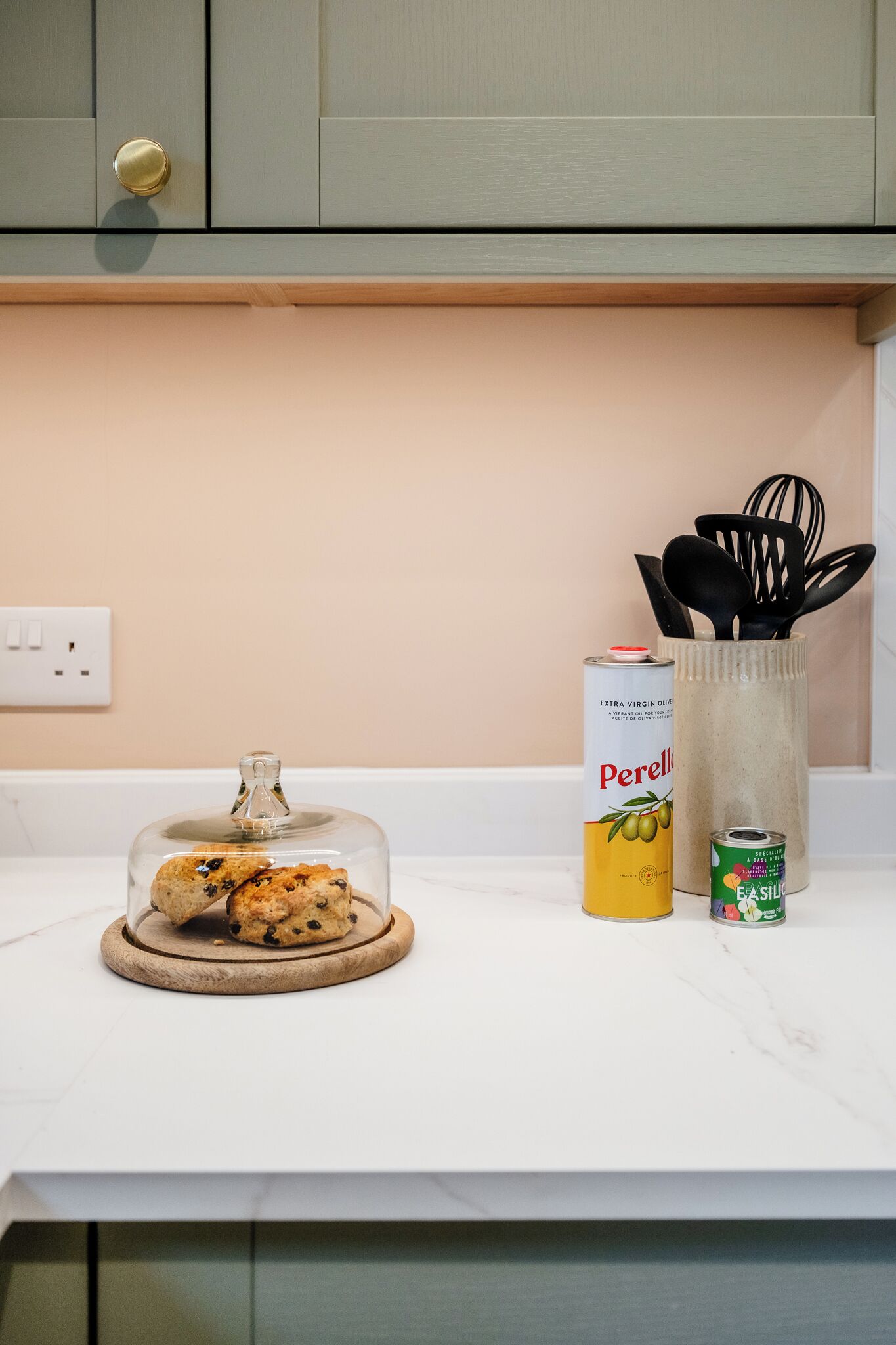 A kitchen counter with a glass dome containing cookies, a can of Perelle, and a can of FASILLO.