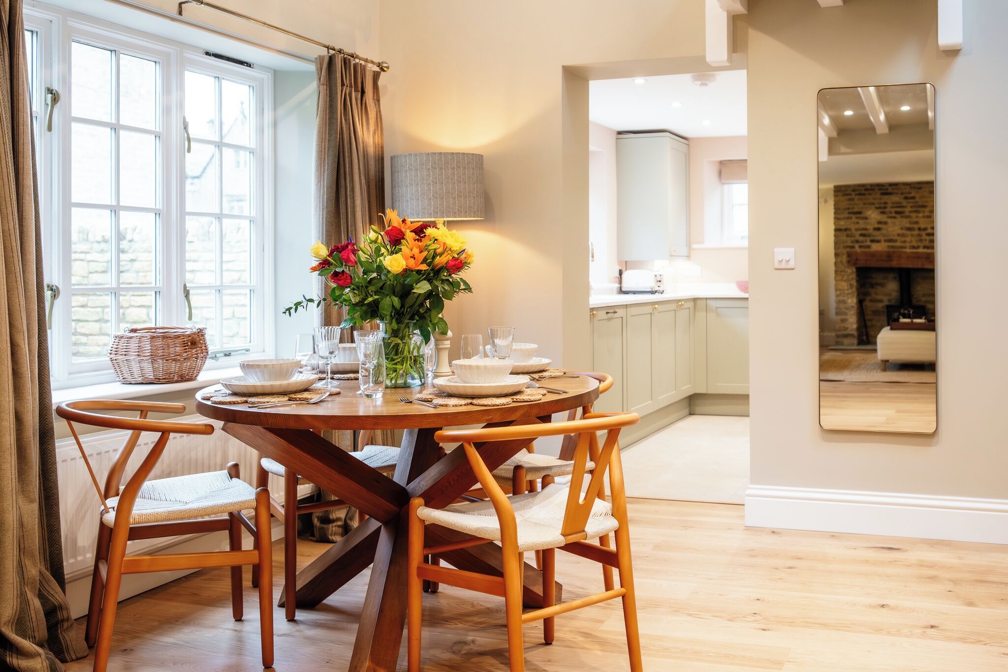 A dining area with a round table, chairs, a vase of flowers, and a view of the kitchen and living area.