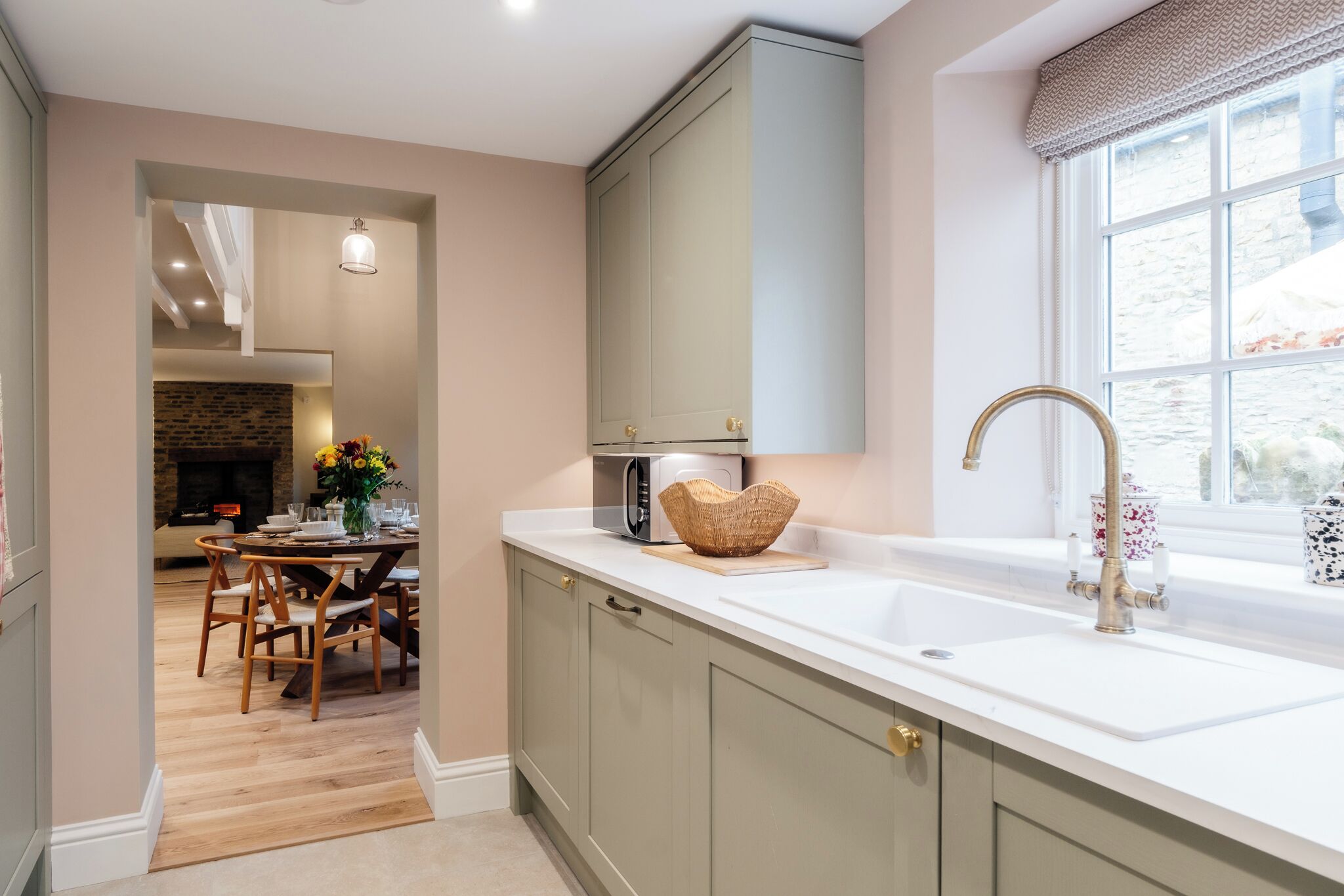 A kitchen with a white countertop, a built-in microwave, a sink with a gold faucet, and a window with a view of the outside.