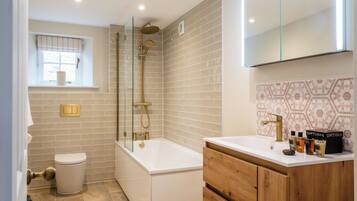 A modern bathroom with a bathtub, toilet, and vanity with toiletries.