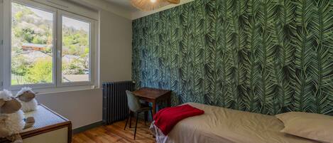 Une chambre à coucher comprenant un lit, un bureau, une chaise, un radiateur et une fenêtre donnant sur un paysage verdoyant.