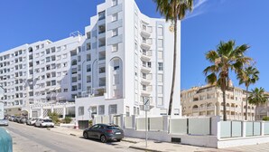 A multi-story hotel with balconies, a parking area, and palm trees. - Beachfront Apartment with Pool, High-Speed Wi-Fi, and Air Conditioning (Almuñécar)