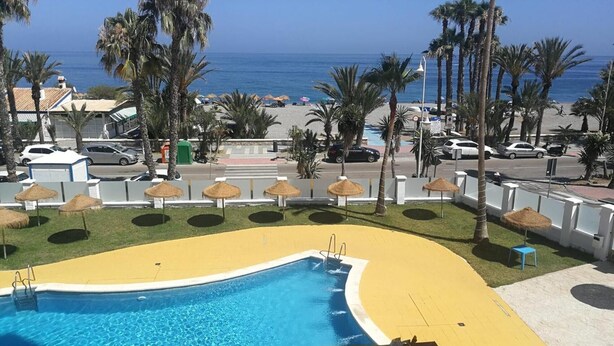 A pool area with a yellow border, palm trees, and a view of the beach and ocean. - Beachfront Apartment with Pool, High-Speed Wi-Fi, and Air Conditioning (Almuñécar)