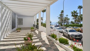 A covered outdoor area with a checkered floor, potted plants, and a view of parked cars and palm trees. - Beachfront Apartment with Pool, High-Speed Wi-Fi, and Air Conditioning (Almuñécar)