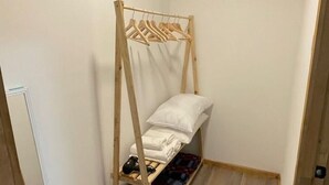 Ein kleiner, schmaler Raum mit einem Holzbett, einem Wäscheständer aus Holz und einem kleinen Tisch mit Stuhl.