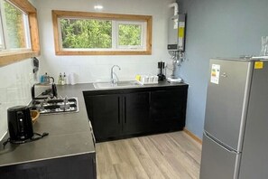 Eine kleine Küche mit Spüle, Herd und Kühlschrank, Holzboden und einem Fenster mit Blick auf Grünflächen.