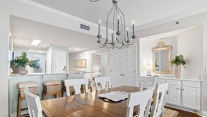 Ein Essbereich mit Holztisch, weißen Stühlen, einer Chandelierleuchtre und weißen Schränken.
