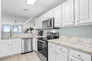 A modern kitchen with white cabinets, stainless steel appliances, a granite countertop, and a view to the outside. - New Rental! Gulf Front Paradise at Palacio 1002! (Perdido Key)