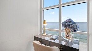 Ein Schreibtisch mit Lampe und Blumen in einer Vase an einem Fenster mit Blick auf das Meer.