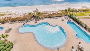 Ein Poolbereich mit mehreren Schwimmbecken, Liegestühlen und einem Strand im Hintergrund.