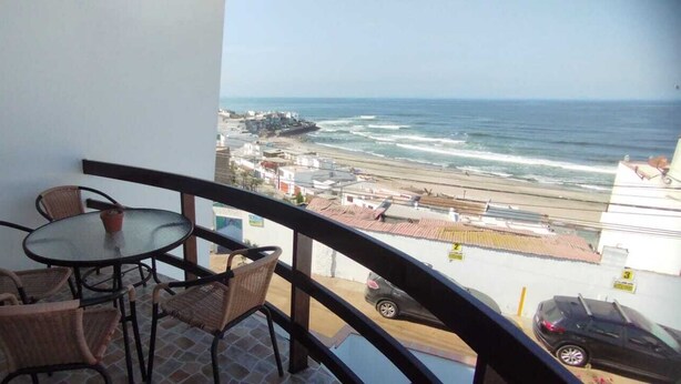 Un balcone con sedie in vimini e un tavolo, affacciato su una spiaggia e l'oceano.