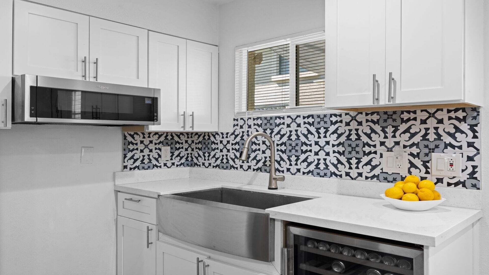A kitchen with white cabinets, a stainless steel sink, a microwave, and a patterned backsplash.
