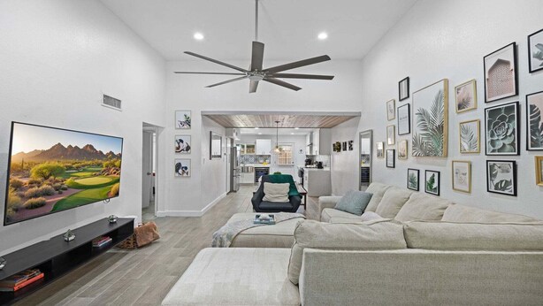 A modern living room with a flat-screen TV, a ceiling fan, and a dining area with a kitchen in the background. - Eden's Escape Comfort, Style & Prime Phoenix Location (Phoenix)