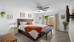 A bedroom with a bed, bedside table, bench, ceiling fan, and a TV mounted on the wall. - Eden's Escape Comfort, Style & Prime Phoenix Location (Phoenix)