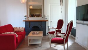 A living room with a red sofa, a wooden coffee table, and a red armchair. A fireplace is visible in the background.