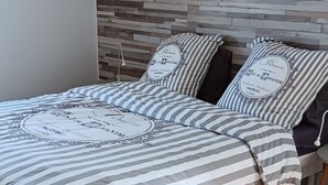 A modern bedroom with a wooden headboard, striped bedding, and a hanging light fixture.