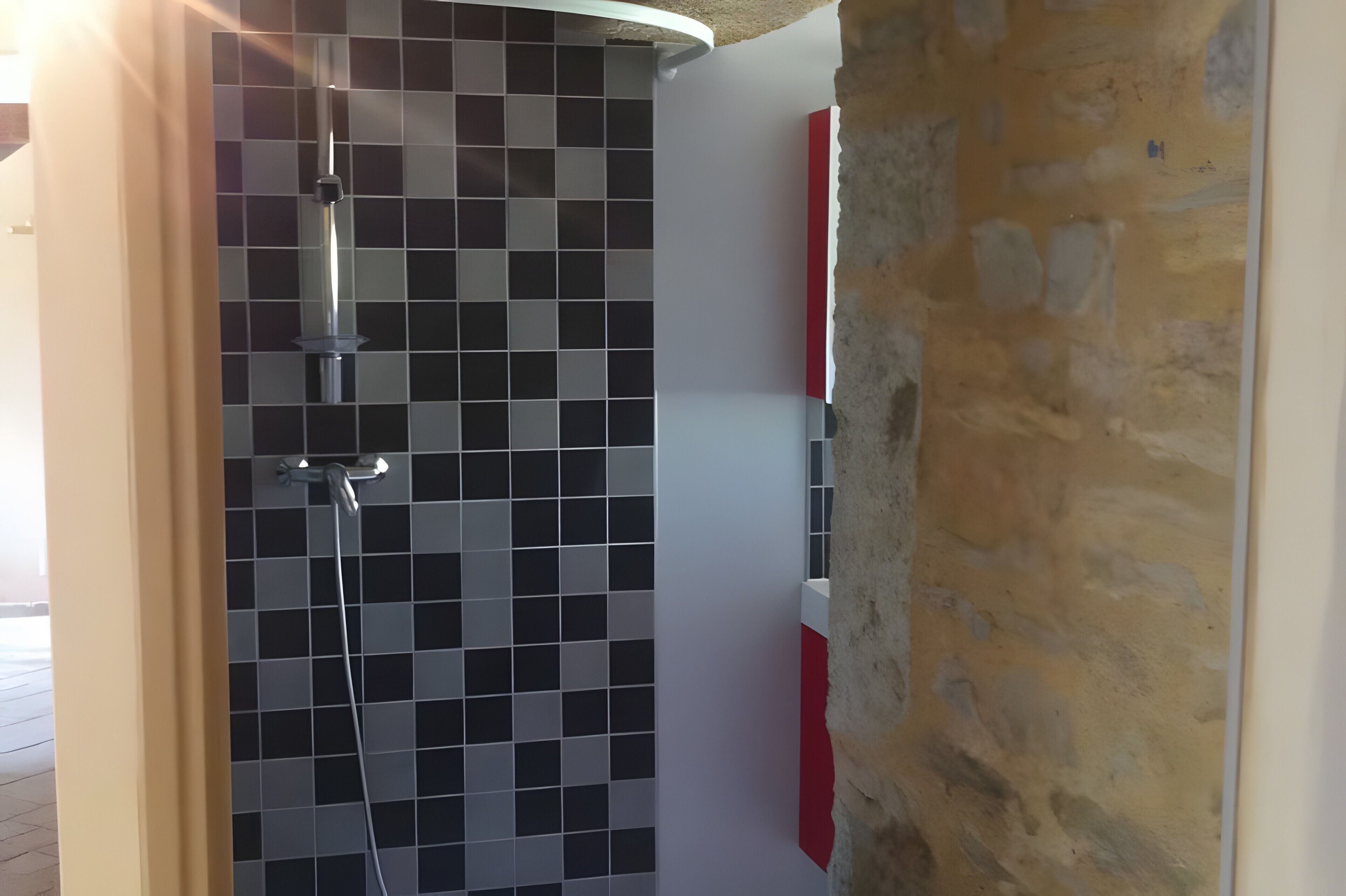 Un baño con pared de ducha en cerámica, una puerta blanca y una pared de piedra.