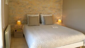 Een slaapkamer met een stenen muur, een bed met twee kussens, een nachtkastje met een lamp en een radiator.