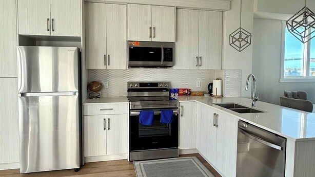 Une cuisine moderne dotée d’appareils électroménagers en acier inoxydable, de meubles blancs et d’un plancher en bois.