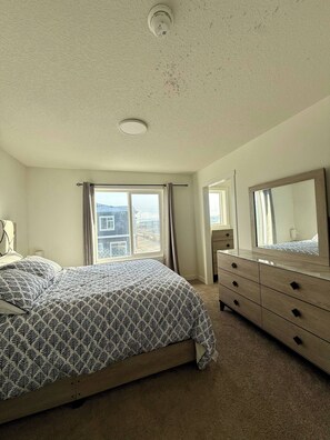 A bedroom with a bed, dresser, and window. - Modern Living - Corner Unit Townhome 3 Bedrooms (Calgary)