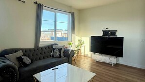Un salon moderne avec un canapé, une table basse, un téléviseur à écran plat et une fenêtre avec des rideaux.